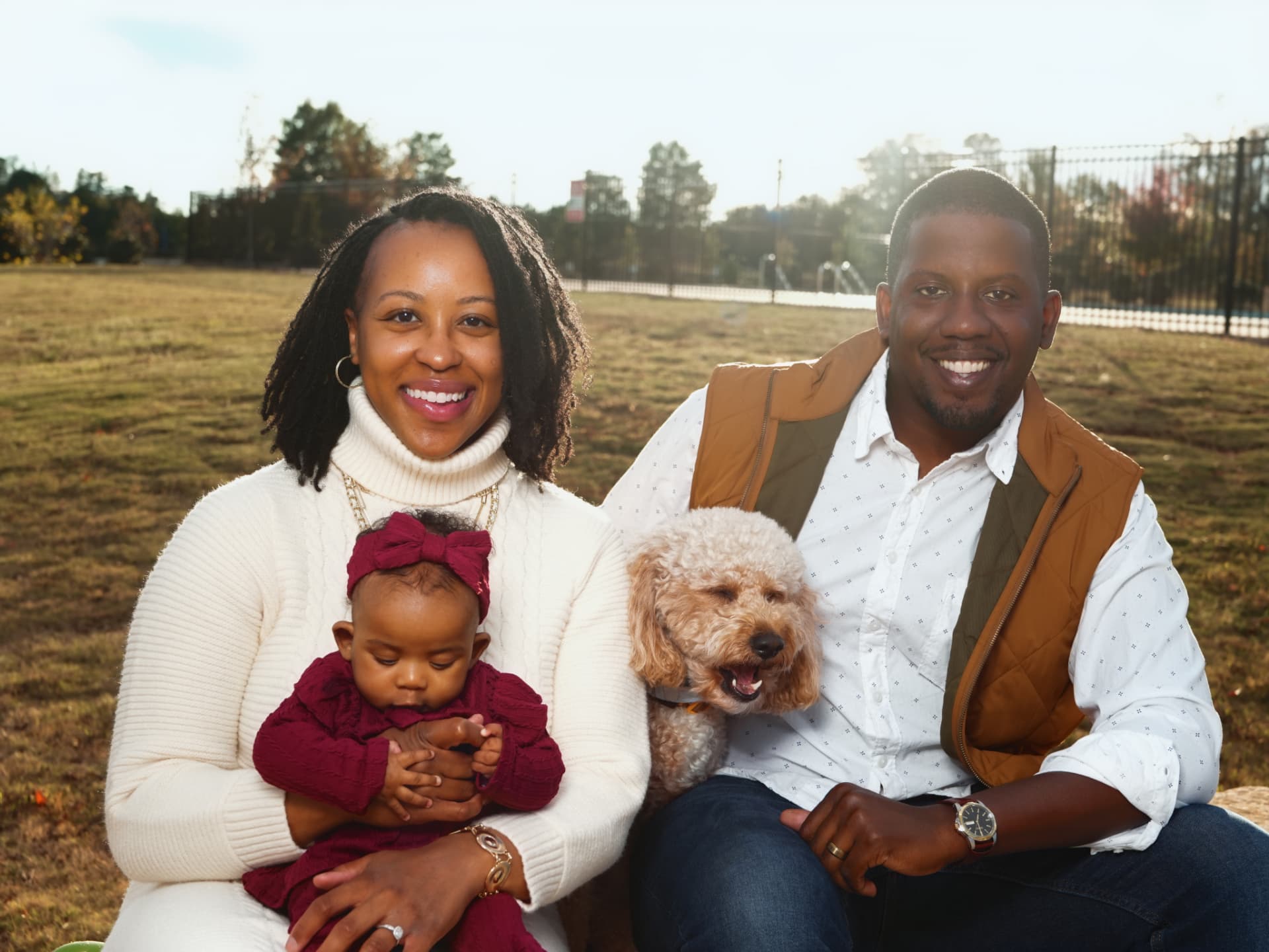 A family of three with their small dog smiling together on a golden lawn