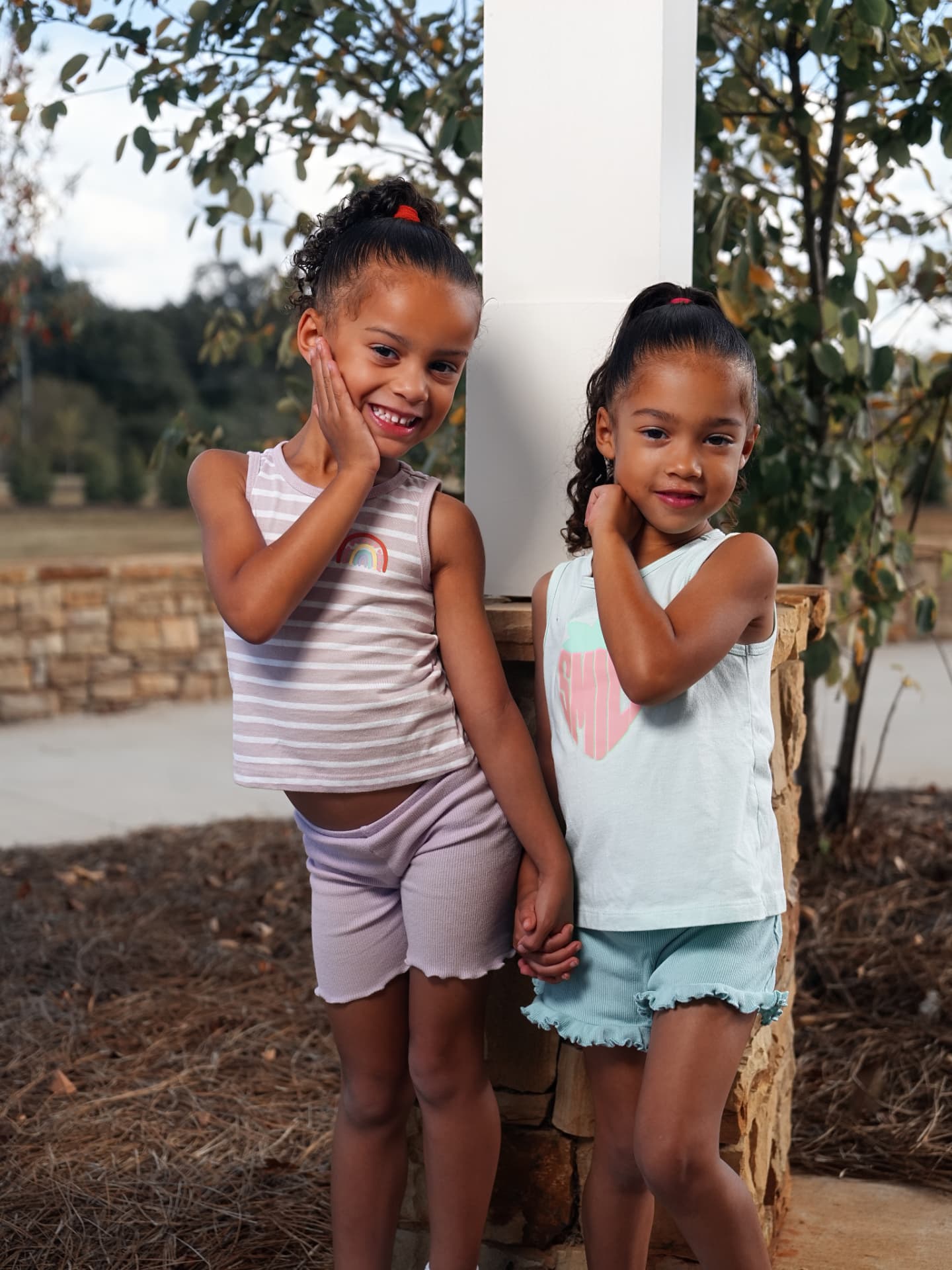 Two young sisters holding hands and posing beside a community pavilion column