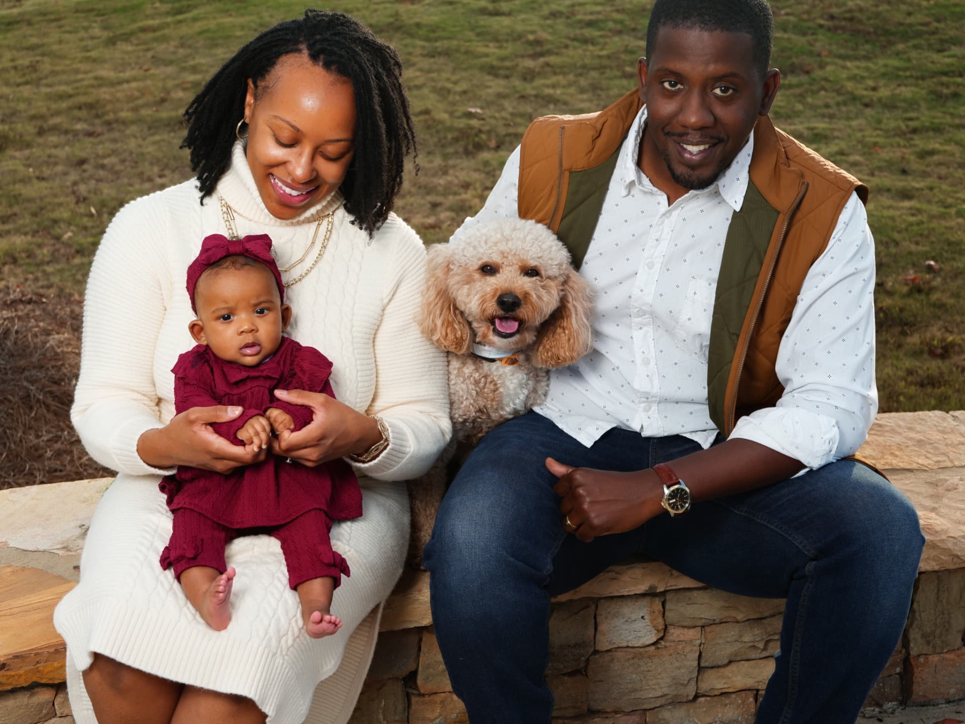 A family seated close together on a stone wall with their baby and dog during a community portrait session